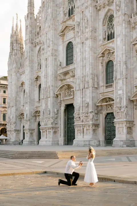 Uomo in ginocchio con l'anello davanti a una ragazza in abito bianco nella Piazza del Duomo di Milano deserta